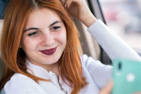 Young Redhead Woman Driver Taking Selfies With Her Mobile Phone Sitting Behind The Wheel Of The