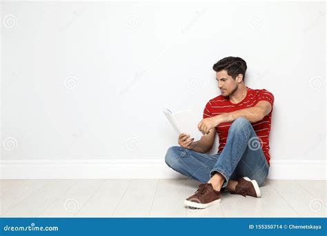 Handsome Man Reading Book On Floor Near White Wall Stock Photo Image