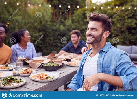 Portrait Of Man With Friends At Home Sitting At Table Enjoying Food At Summer Garden Party Stock