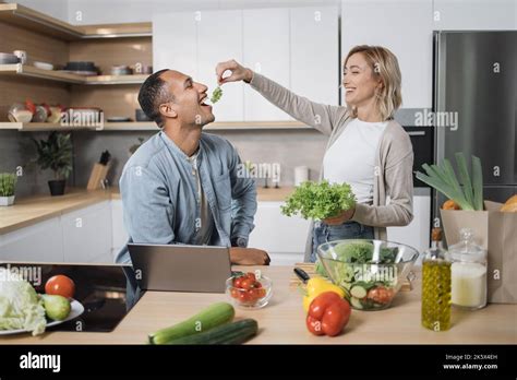 cheerful married multinational couple using laptop while cooking