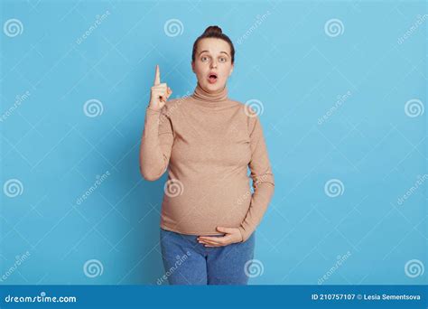 surprised pregnant woman pointing finger up isolated over blue background keeps mouth opened