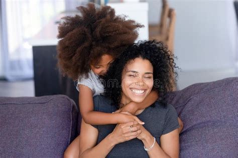 Niña Negra Abraza A Mamá Sonriente En El Sofá Por Detrás Foto De