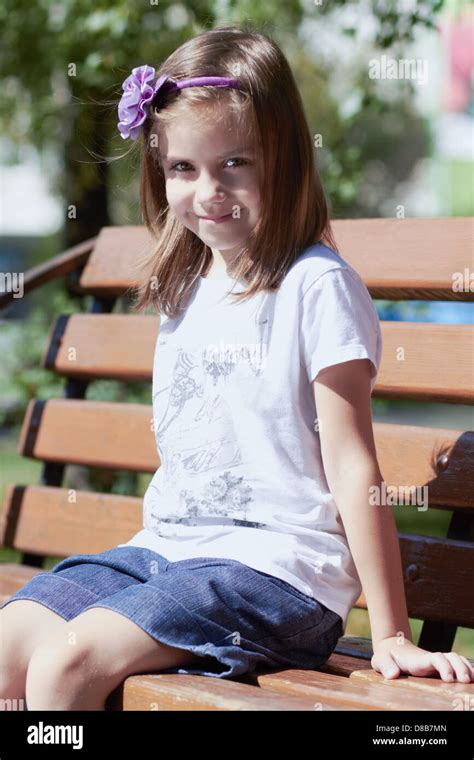 Pretty Kid Posing On A Bench Outdoors In A Bright Sunny Day Stock Photo