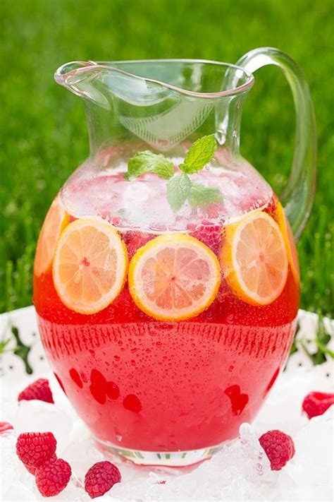 A Pitcher Filled With Liquid And Sliced Lemons On Top Of A White Table