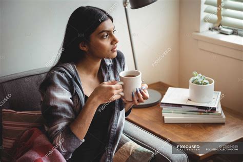 Woman Holding Cup Of Coffee Looking Through Window At Home — Morning