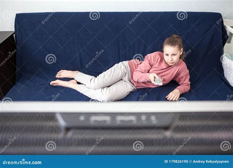 Pre Teen Age Girl Watching Television Lying On Couch With Tv Remote Control Wide Screen Is On