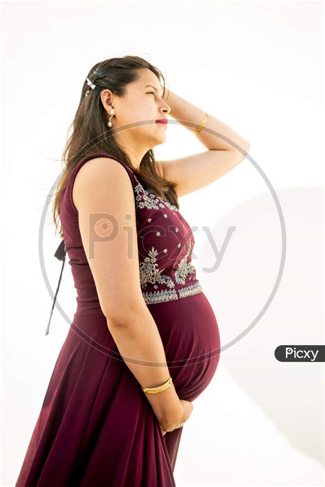 Image Of Young Asian Indian Pregnant Woman Looking At Belly Standing Against White Background