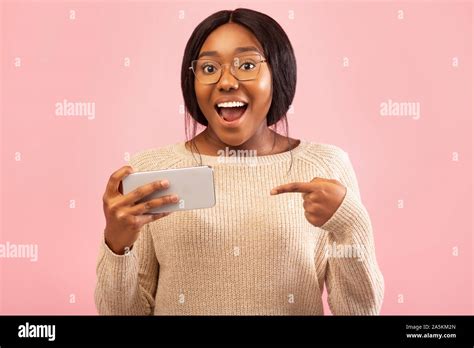 Excited Black Woman Pointing Finger At Cellphone Standing Pink