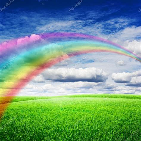 Green Field Under Blue Clouds Sky With Bright Rainbow