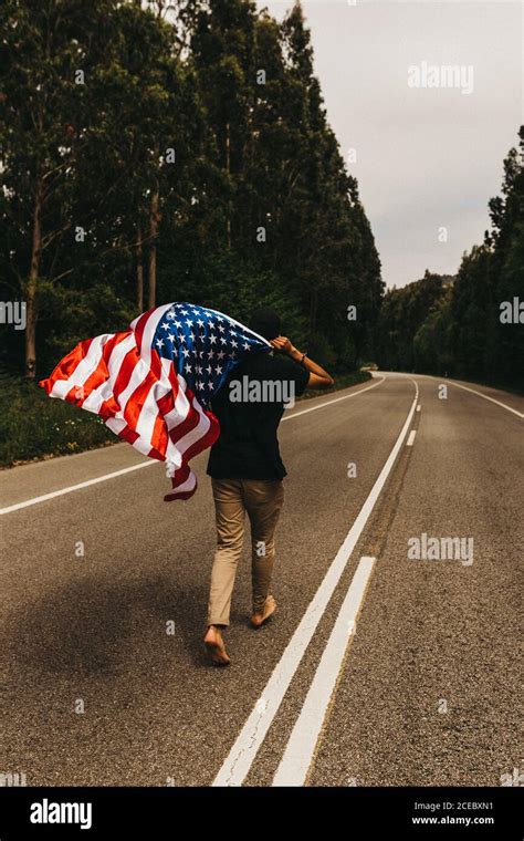 Back View Of Barefoot Man Holding Flag Of Usa And Running Along Narrow