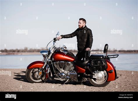 Full Length Portrait Of Biker Standing By Motorcycle And Looking Away