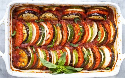 A Casserole Dish Filled With Sliced Vegetables And Sauce On The Side