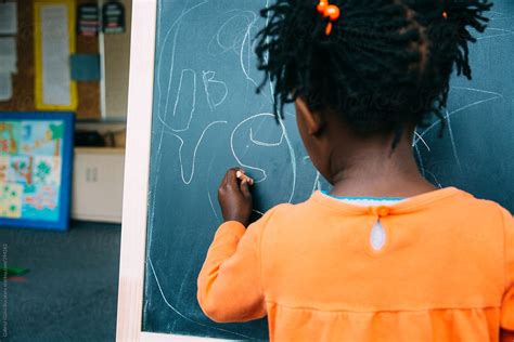 African American Girl Writing At A Blackboard In A Kindergarten Class Del Colaborador De