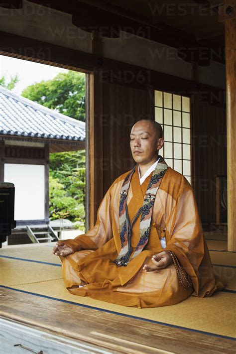 Buddhist Monk With Shaved Head Wearing Golden Robe Sitting Cross Legged
