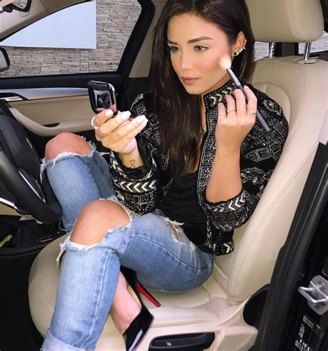 A Woman Sitting In The Back Seat Of A Car Using Her Cell Phone And Makeup Brush