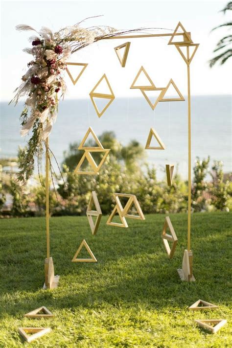 A Geometric Ceremony Backdrop With Floating Gold Triangles Is A Nod To