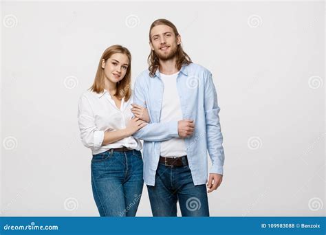 Portrait Of Attractive Young Couple Smiling For The Camera While Holding Arm To Arm On Grey