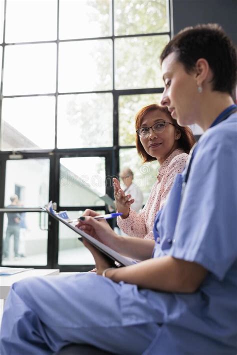 Woman Nurse Consulting Asian Patient In Hospital Lobby Stock Photo
