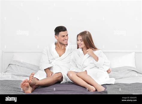 Young Loving Couple In Bathrobes Relaxing On Bed At Hotel Stock Photo