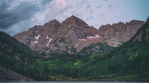 Two Red Hued Mountain Peaks Towering Above A Green Forest And A Lake In