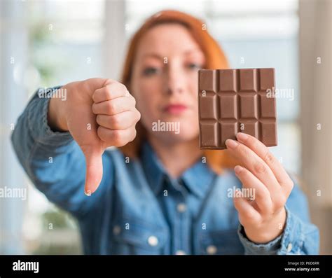Redhead Woman Holding Chocolate Bar At Home With Angry Face Negative