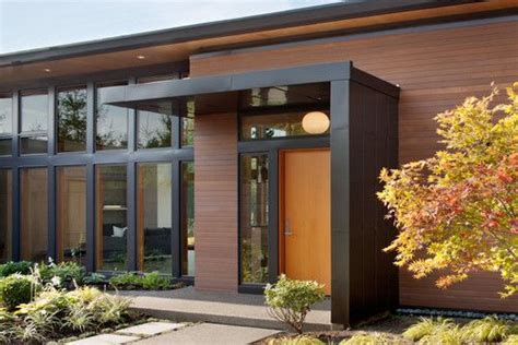 A Modern House With Wood Siding And Glass Windows On The Front Door Is