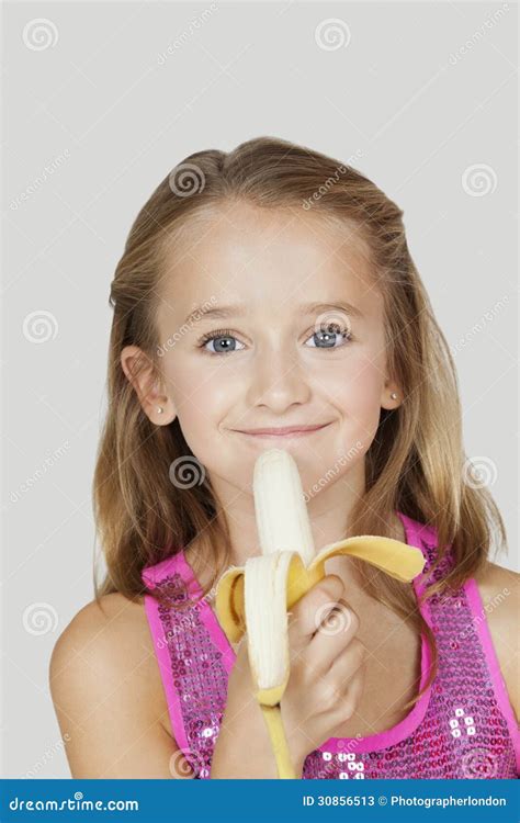 Portrait Of Young Girl Holding Banana Against Gray Background Stock