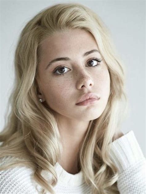 a woman with long blonde hair wearing a white sweater and looking off to the side