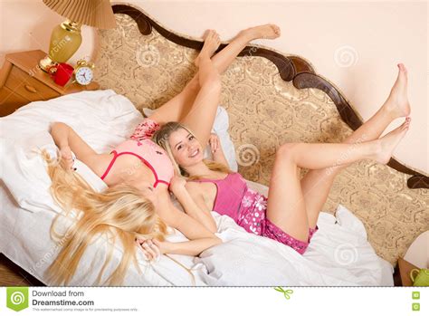 Two Adult Sisters In Pajamas Lying On White Bed Stock