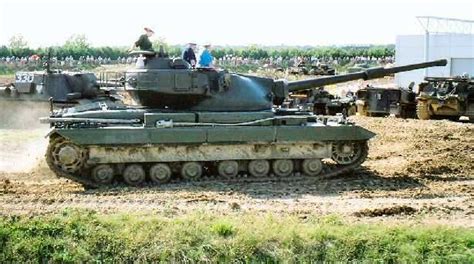 People Are Sitting On Top Of An Army Tank In The Middle Of A Dirt Field