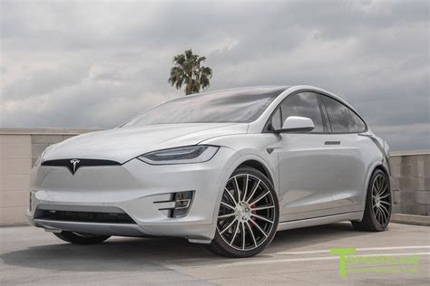 A White Tesla Model X Parked In A Parking Lot Next To A Concrete Wall