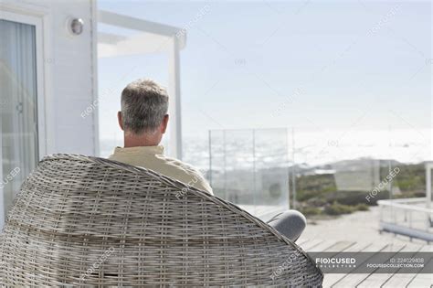 Man Relaxing In Wicker Chair On Terrace Of House House On Sea Coast — Furniture People Stock