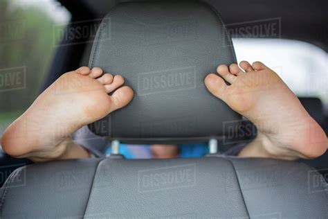 A Child In The Backseat Of A Car Wraps His Feet Round The Front Seat