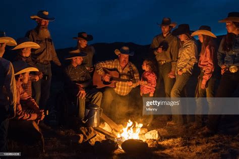Large Group Of Cowboys Singing And Playing Guitar At Campfire High Res