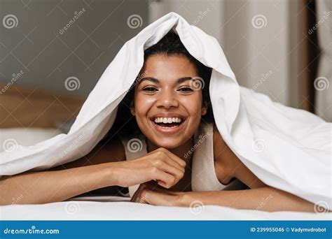 Happy Young African Woman Laying Hiding Under Blanket Stock Photo