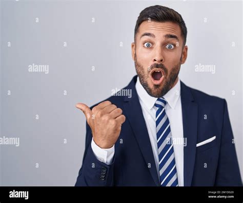 Handsome Hispanic Man Wearing Suit And Tie Surprised Pointing With Hand Finger To The Side Open