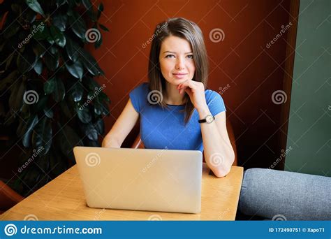 A Beautiful Girl Sits In A Cafe Dressed In A Blue Dress Behind A Laptop