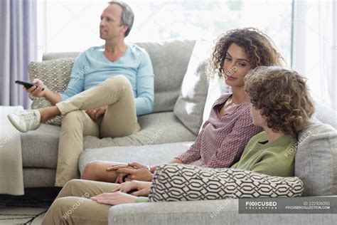 mother talking to son on sofa while father watching tv on background in living room at home