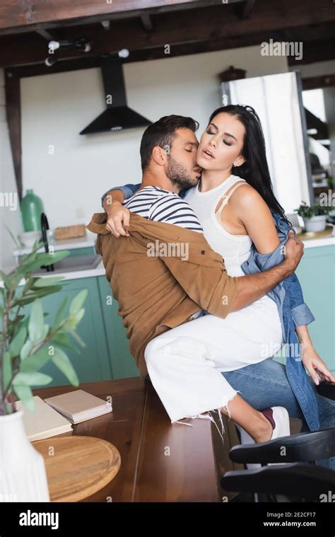 Young Couple In Stylish Casual Clothes Undressing Each Other In Kitchen Blurred Foreground