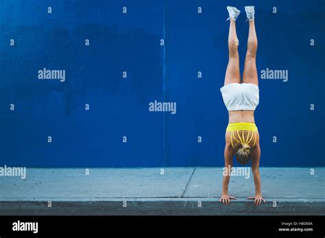 Young Woman Doing Handstand Outdoors In Front Of Blue Wall Stock Photo