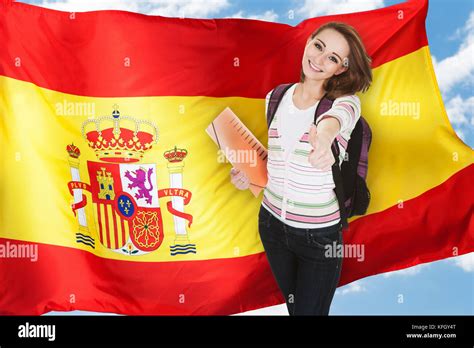 Young Spanish Female Student Gesturing Thumb Up In Front Of Spain Flag