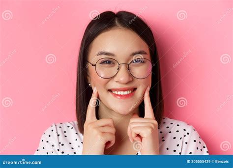 beauty concept headshot of adorable asian girl in trendy glasses smiling poking cheeks and