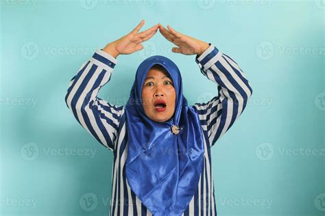A Surprised Middle Aged Asian Woman In A Blue Hijab And Striped Shirt