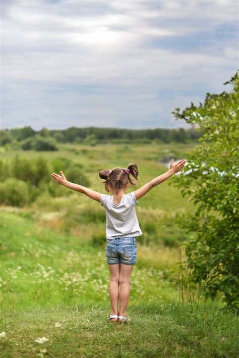 een kleine meisjeszitting op een groene hiel terug naar de kijker met haar handen omhoog en