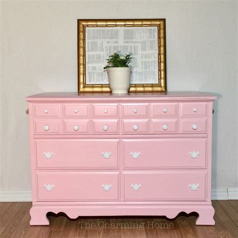 A Pink Dresser With A Potted Plant On Top And A Gold Frame Above It