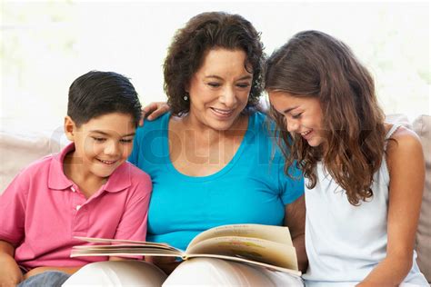Grandmother Reading With Grandchildren At Home Together Stock Image