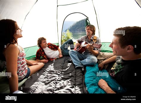 Young Adults Camping Listen To A Friend Play Guitar Inside The Tent