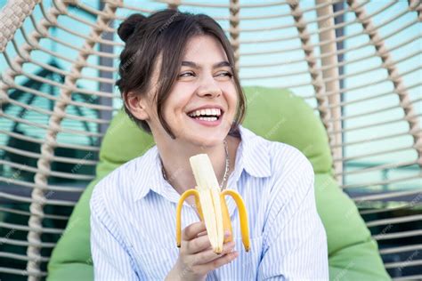 Heureuse Jeune Femme Mangeant Une Banane Assise Dans Un Hamac Photo Gratuite