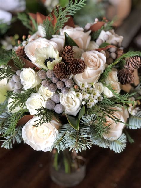 A Vase Filled With White Flowers And Pine Cones On Top Of A Wooden