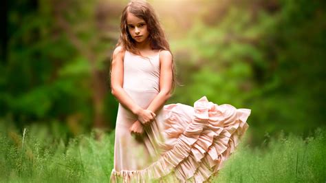 Cute Little Girl Is Standing In Green Trees Background Wearing Peach